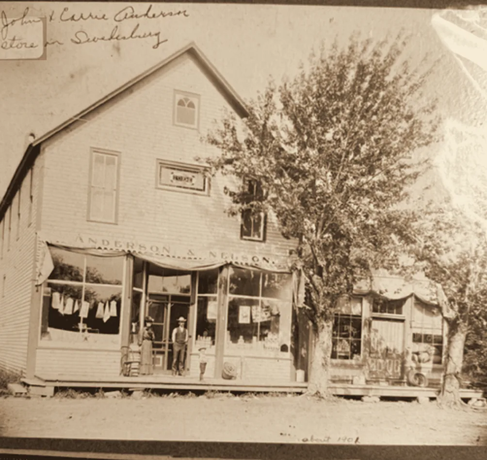 Sepia photograph, fall 1901, of the Anderson & Nelson general store in Swedesburg, Iowa, with people, including a little boy, standing on the front porch.