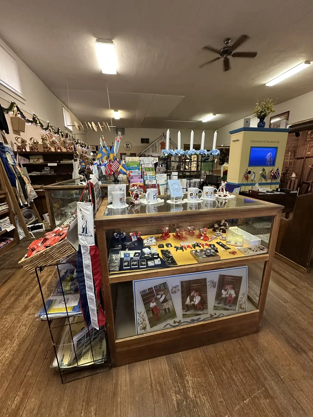Inside the museum's Scandinavian gift shop: a glass display case with FIKA mugs, small Dala horses and an Advent candle arch, surrounded by flags and cards.