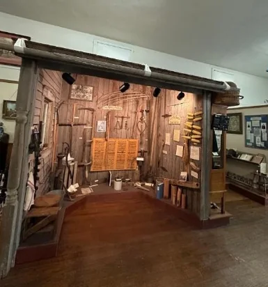 A pioneer workshop exhibit with hand tools hanging on weathered wooden walls.