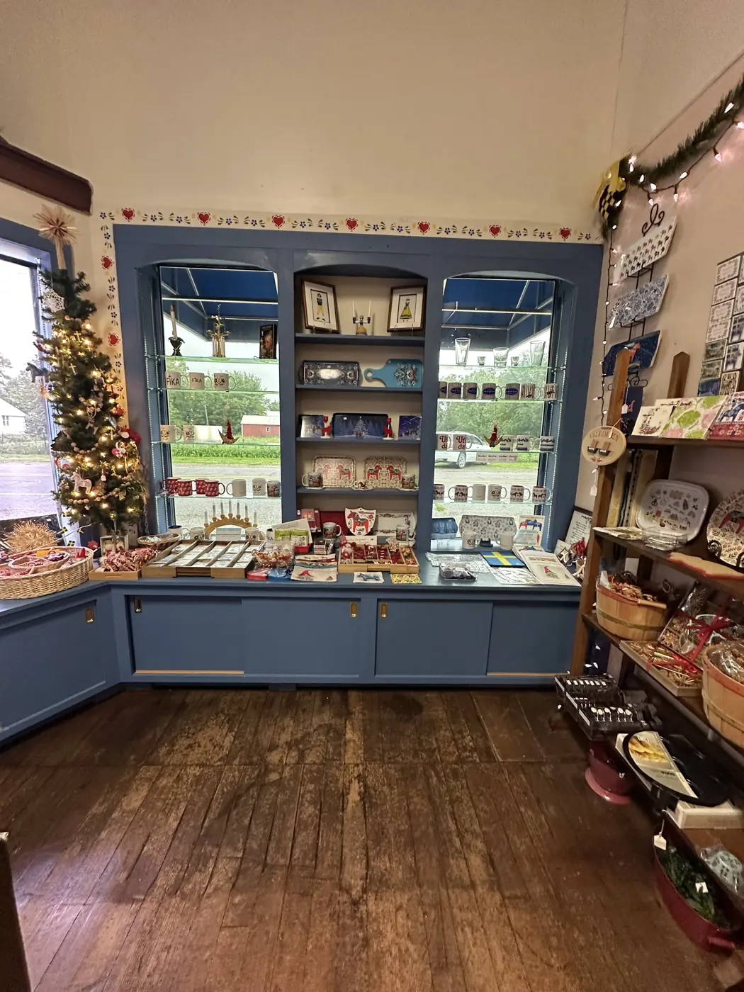 Inside the museum's Scandinavian gift shop: blue built-in shelves of mugs and plates, a candle arch, straw ornaments and a decorated Christmas tree.